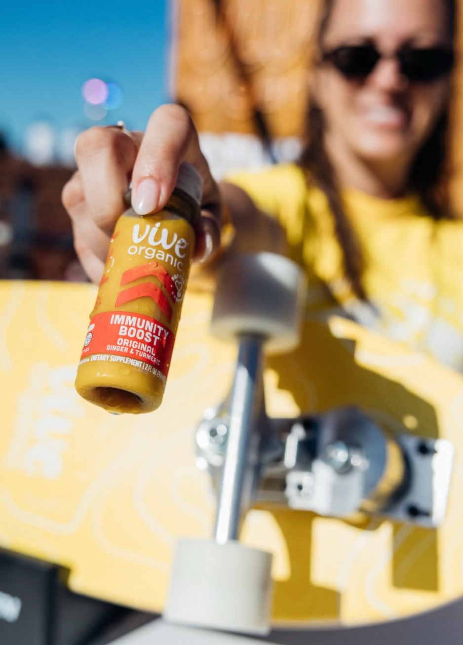 Shot Vive Organic em primeiro plano, com pessoa e skate ao fundo.